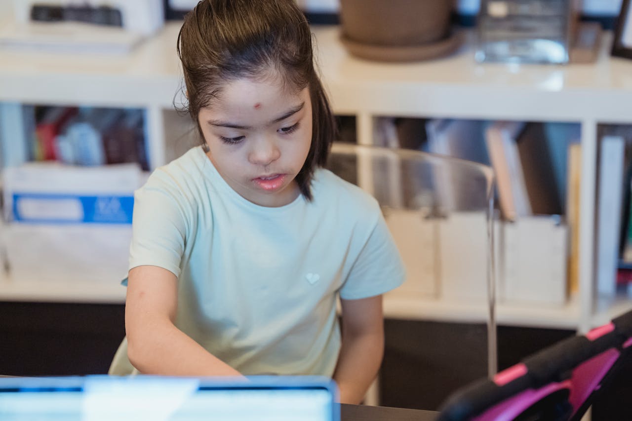 A young girl with Down syndrome focused on a tablet inside a cozy home setting.